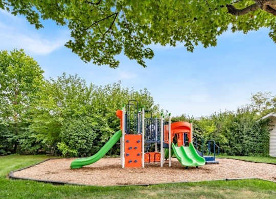 Playground with a green slide and orange and red climbing structure at Versailles, 25026 E Rue Versailles, Oak Park, MI