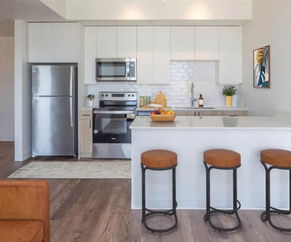 A kitchen with stainless steel appliances, marble countertops, barstools, and large white cabinets at Joy on 4th. 