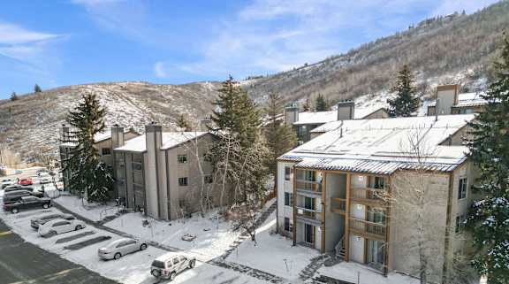 A snowy parking lot with cars and a building in the background.