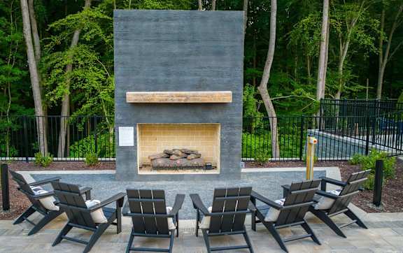 A fireplace with a stone surround and a wooden mantle is surrounded by four chairs.