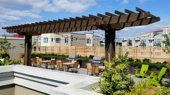 A patio with a wooden pergola and green chairs.