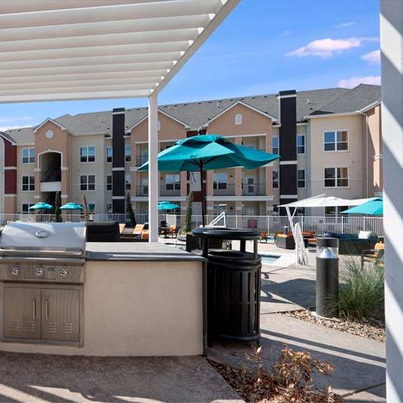 The outdoor grilling area with grills, turquoise umbrellas, and chairs in the background at Latitude 31 Resident Lounge. 
