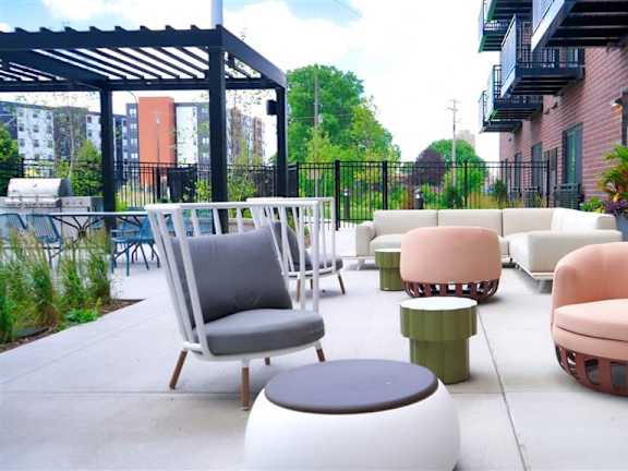 A patio with a black metal awning and a variety of seating options including a pink chair and ottoman at The Bessemer at Seward Commons Apartments, Minneapolis, Minnesota