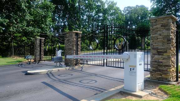 a gate with a white box in front of it and a street with trees in the background