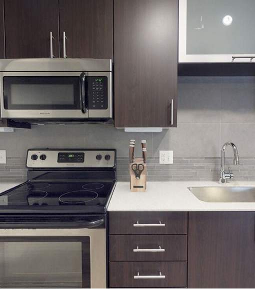 A modern kitchen with a stove, microwave, and sink.at The Logan Apartments, Colorado