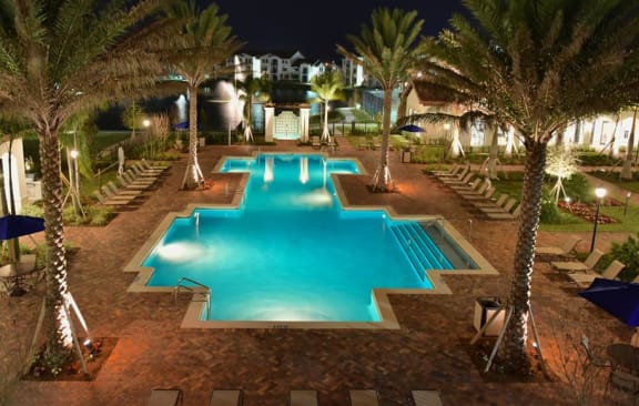 a large swimming pool surrounded by palm trees at night at The Atlantic at Tradition, Port St Lucie, FL, 34987