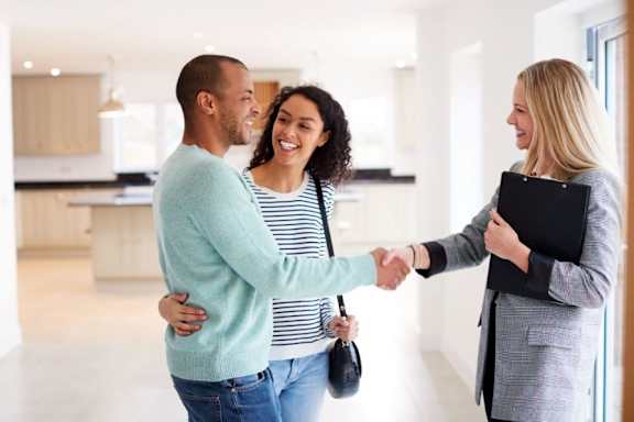 A real estate agent shakes hands with a couple in a modern kitchen.