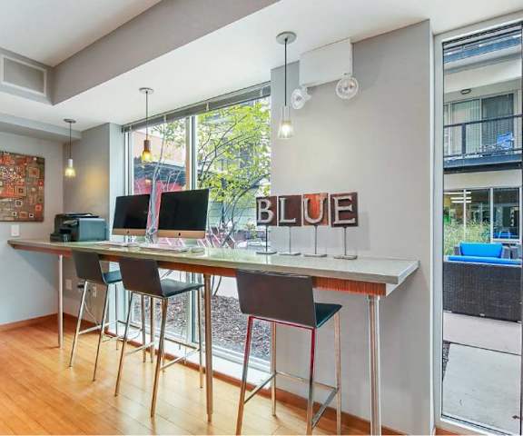 A business center with a table and chairs against the wall facing windows with computer monitors and a printer at Blue and Lime Apartments. 