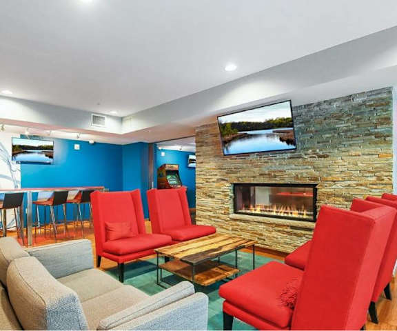 The resident lounge with a fireplace, tv, plush chairs, a couch, a coffee table, and a long high table with barstool chairs at Blue and Lime Apartments. 
