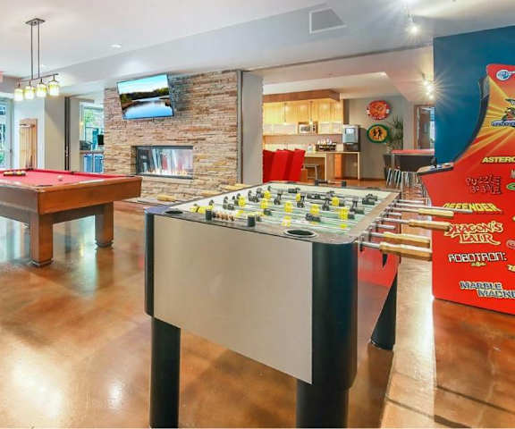 Lounge with games such as foosball, pool, and arcade games, as well as tables, chairs, and a community kitchen at Blue and Lime Apartments. 