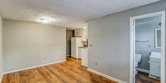 A room with wooden floors and a white ceiling with a kitchen area visible through the door.at Waverly Manor Townhomes, Georgia, 30071