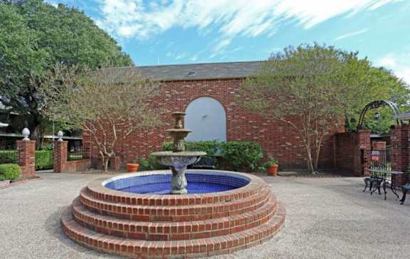 A brick wall with a fountain in the middle of a gravel area.