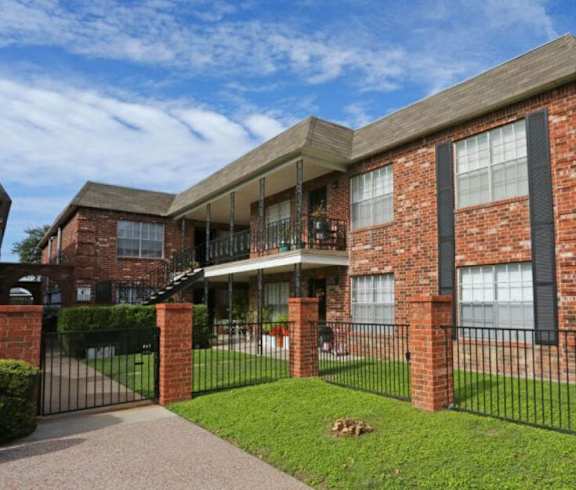 A red brick house with a black fence and a green lawn.