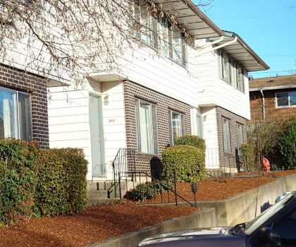 A house with a white front and a brown hedge.