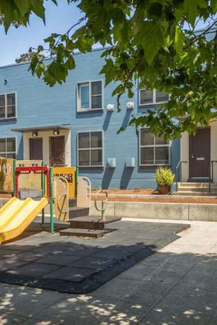A playground with a yellow slide in front of a blue building.
