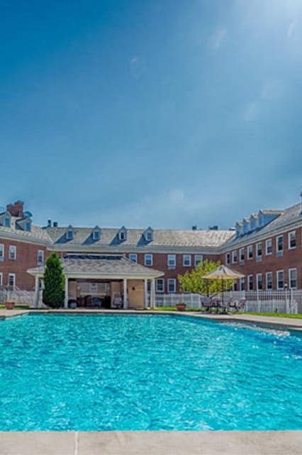 our resort style swimming pool is surrounded by blue chairs and trees