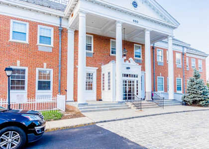 the front of a brick building with pillars and a car parked in front