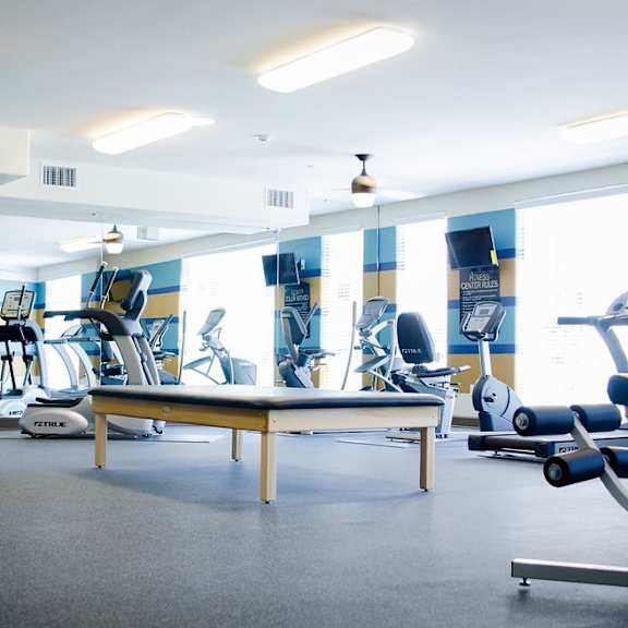A gym with a variety of equipment including treadmills, weights, and a bench.