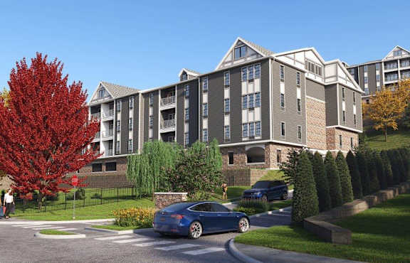 A blue car is parked on the side of a road in front of a large apartment building.