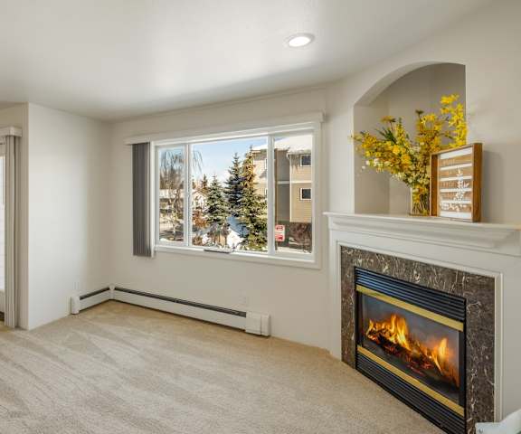 An empty living room with hardwood flooring, windows, and a fireplace with a door to a balcony at La Maisonette. 