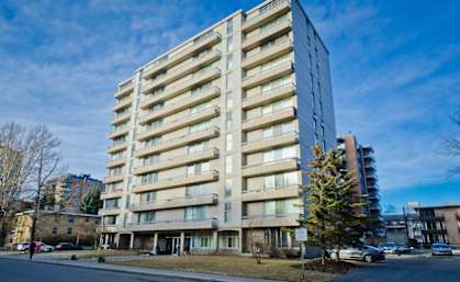 A tall, beige apartment building with a tree in front of it.