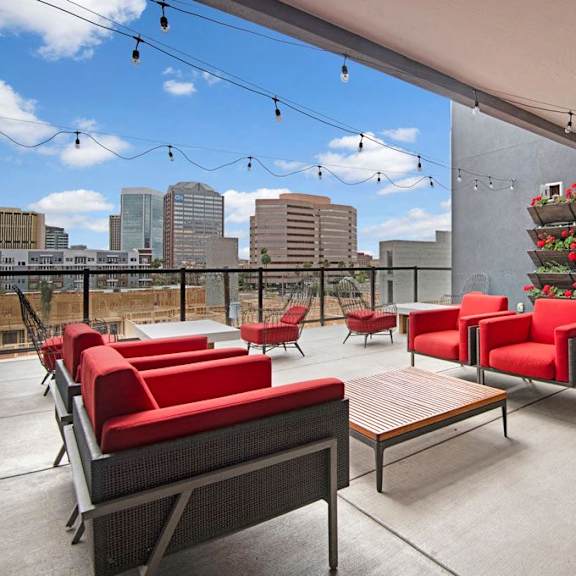 The rooftop patio at Park on Central featuring chairs with plush red cushions, coffee tables, red flowers in wall planters, and a view of the city skyline. 