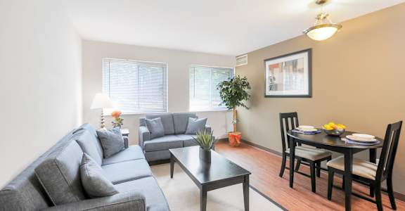 A living room with a grey couch, a black coffee table, and a dining table set for two.