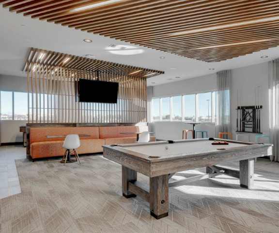 A wonderful resident lounge with tables, chairs, large windows, a TV, and a pool table at the Flats at San Tan Apartment Homes. 