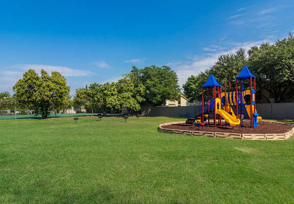 a playground with a swing set in the middle of a grass field at Falls on Clearwood Apartments, Richardson, TX, Texas