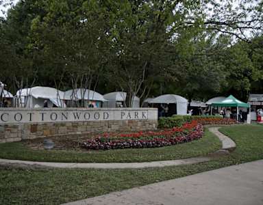 A sign that says Cottonwood Park is surrounded by trees and flowers.