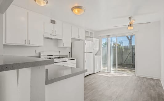 a white kitchen with white cabinets and a sliding glass door at Ocean Villas, Oxnard, CA