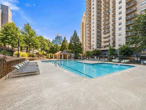 A large swimming pool surrounded by lounge chairs and trees in an urban setting.