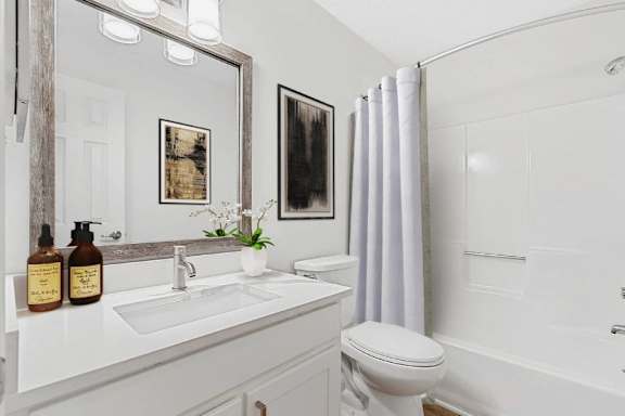 A white bathroom with a toilet, sink, and mirror. at Woodlyn on the Green Apartment Homes, North Carolina