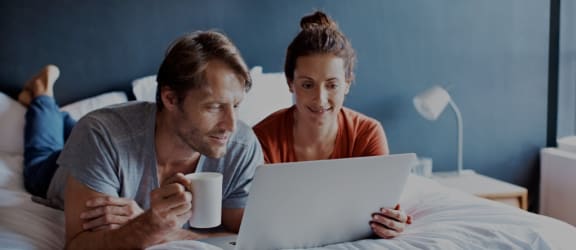 a couple lying in bed looking at a laptop