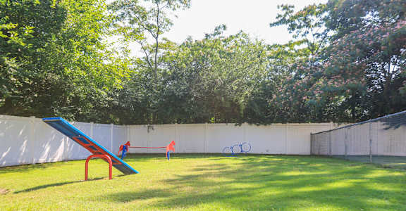 A blue and red slide in a grassy area with trees in the background.