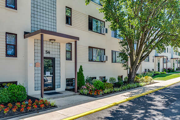 A building with the number 54 on it is surrounded by trees and flowers.