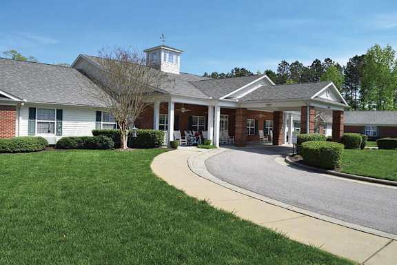 A white building with a tower has a driveway leading to the front door.