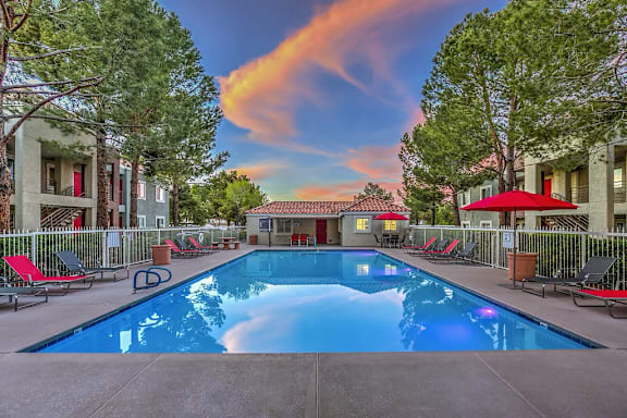 A swimming pool surrounded by red lounge chairs and trees.