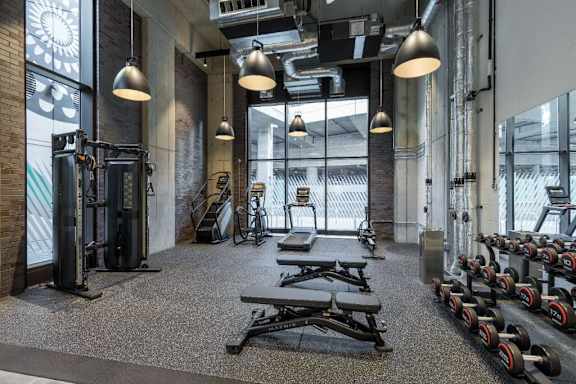 A gym with a variety of equipment including weights and benches at Beton Apartments, Wembley, HA9 0SL
