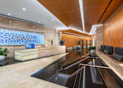 Thumbnail 4 of 15 - A reception area with a blue glass wall and a wooden bench.