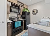 Thumbnail 9 of 27 - Compact kitchen with black appliances and wood style flooring at The Colony Apartments, Universal City, Texas