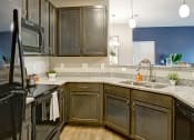 Thumbnail 3 of 21 - Kitchen with dark cabinets, black appliances, sink , granite countertops, and light hard wood flooring at Ascent at Mallard Creek Charlotte, NC