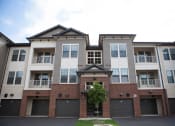 Thumbnail 36 of 36 - Luxury Apartments for Rent in Greenville SC - Velo Verdae - Property Exterior with Brick, White, and Tan Walls, Showcasing Balcony, Street, Garages, and Planted Tree
