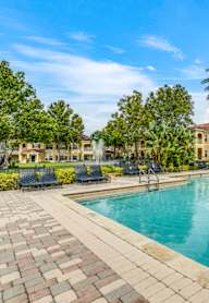A large swimming pool surrounded by a brick patio and palm trees.
