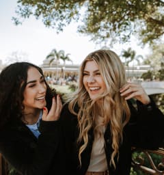 two women laughing while standing in front of a bridge