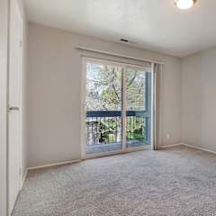 A room with a carpeted floor and a sliding glass door leading to a balcony.