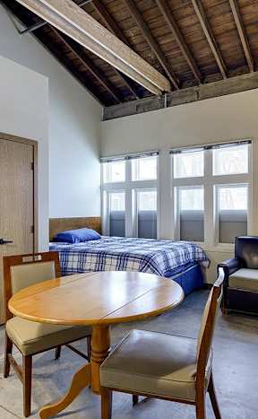 A room with a bed, a chair, a table, and a lamp.