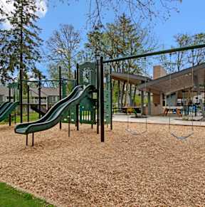 A playground with a green slide and brown sand.