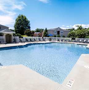 A swimming pool surrounded by a white fence and lounge chairs.