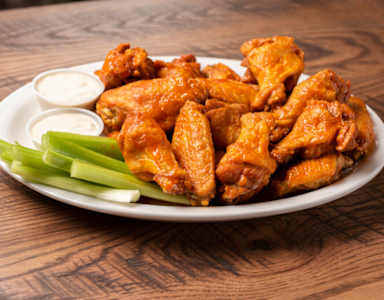 Plate of chicken wings with celery and dipping sauces.